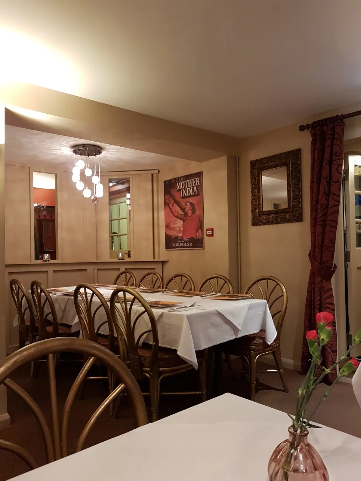 The Masala Lounge dining room at the Golden Lion, with white tablecloths, gold chairs and a Mother India poster